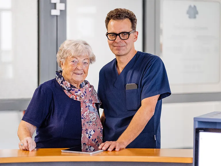 Herr Dr. Reich und eine Patientin lächeln in die Kamera